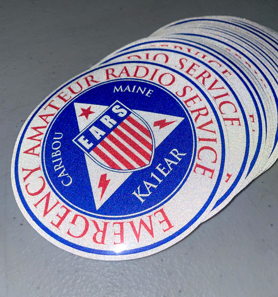 An overlapping fan stack of circular reflective stickers for the Caribou Emergency Amateur Radio Service featuring a blue, white, and red EARS logo design.